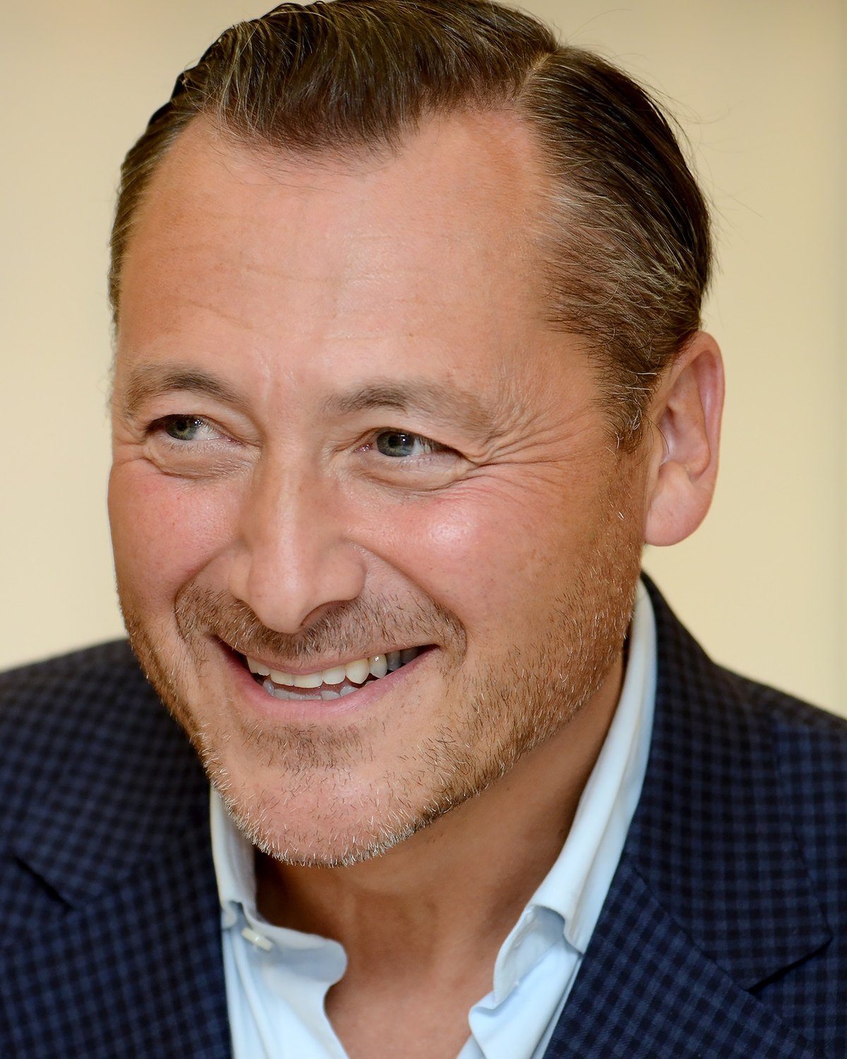 Dan Wagner, smiling, in a navy checked jacket and open-collared white shirt, photographed indoors against a pale background.